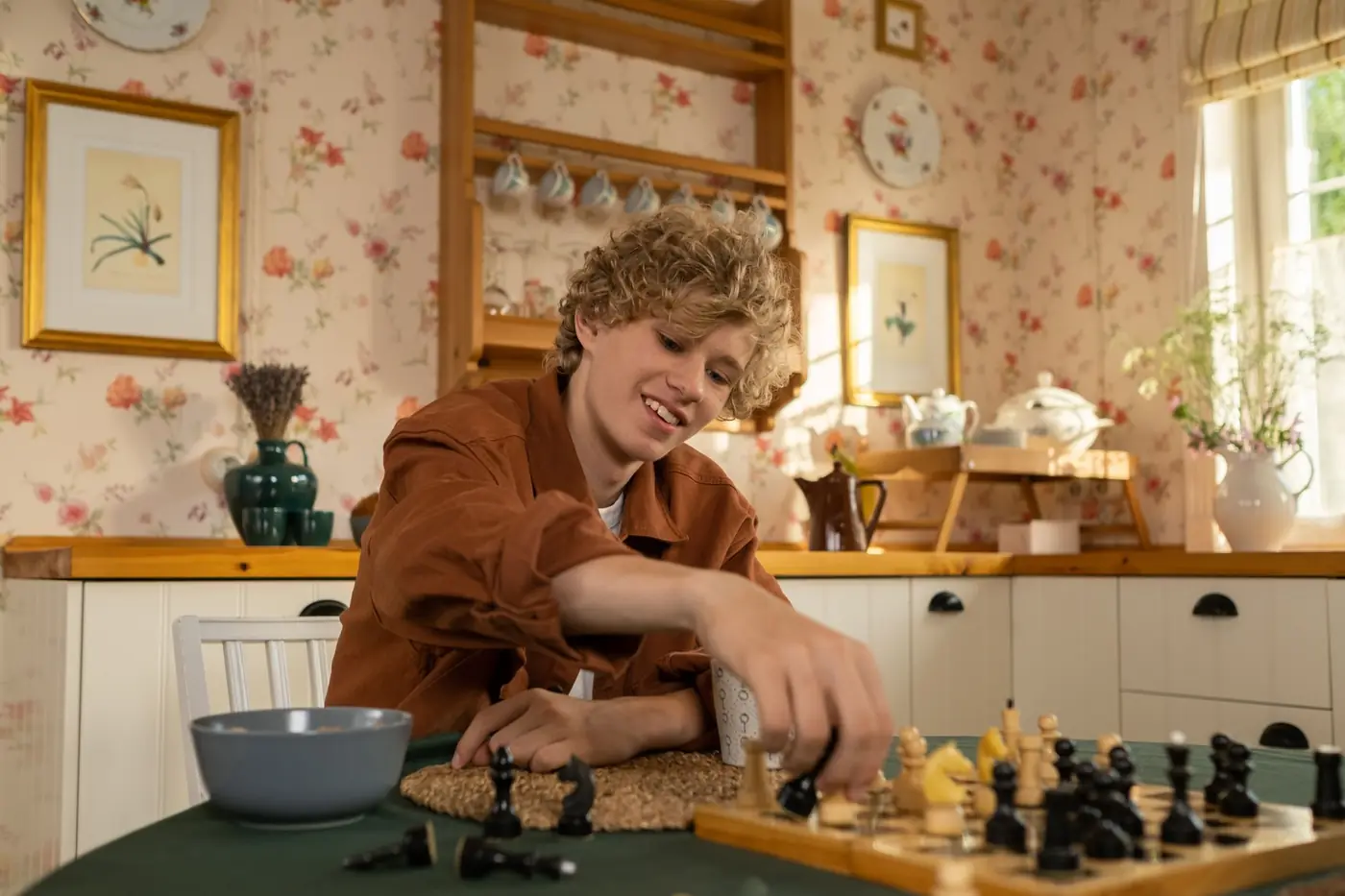 A teenager smiling as he plays chess in a homely kitchen